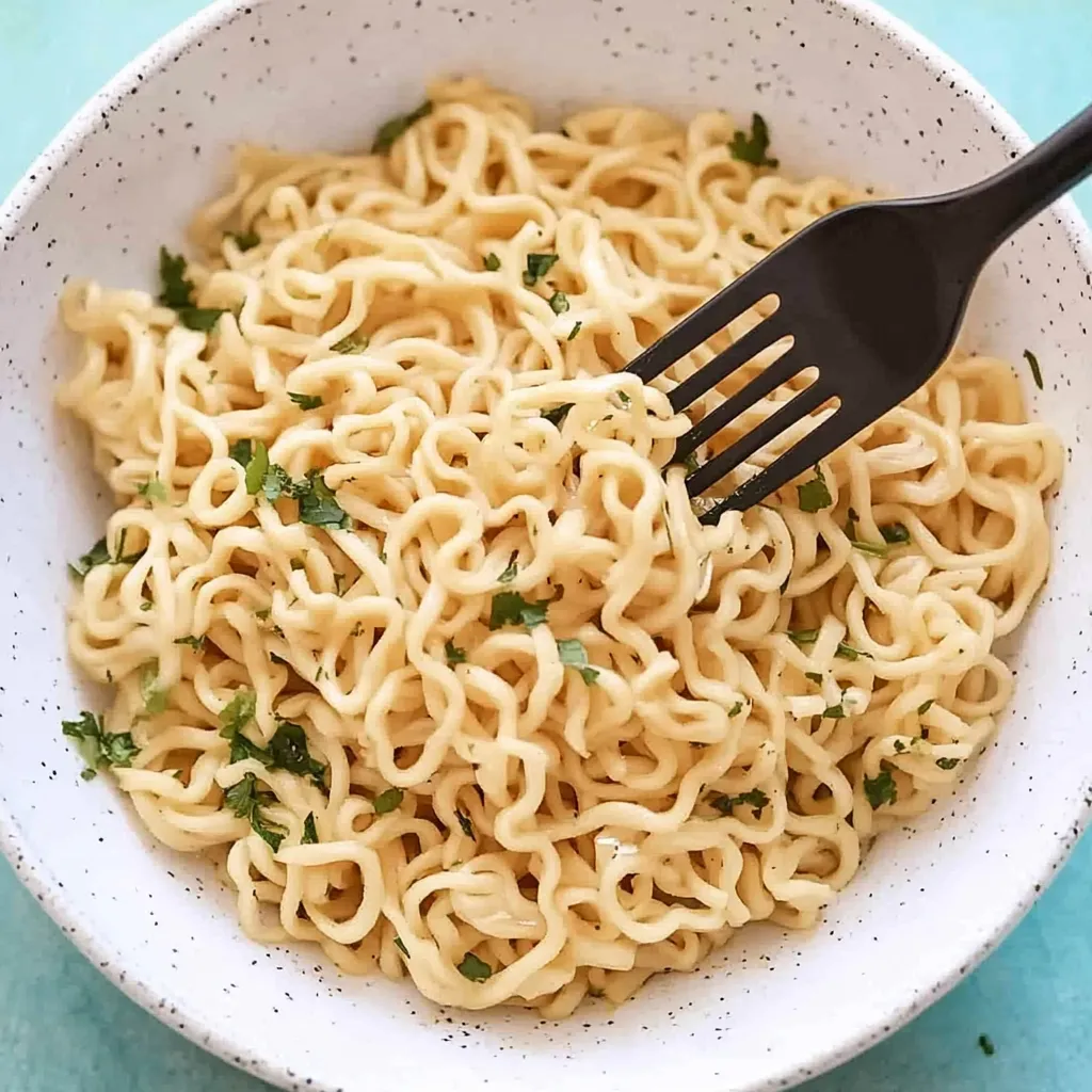 Ein weißer Teller mit Ramen Noodles, die mit Garlic Butter und Zwiebeln garniert sind.
